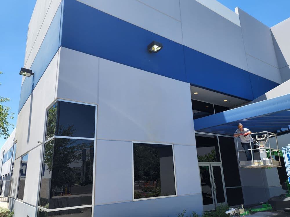 Worker on lift painting the exterior of a modern commercial building with blue accents.