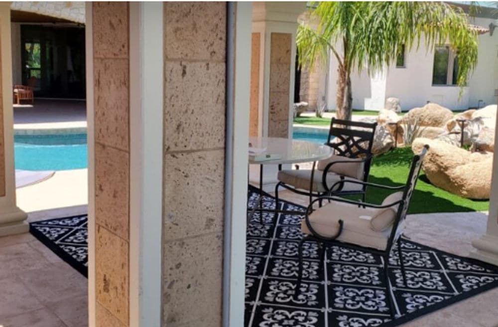 Cozy outdoor seating area by the pool with decorative rug and palm trees.