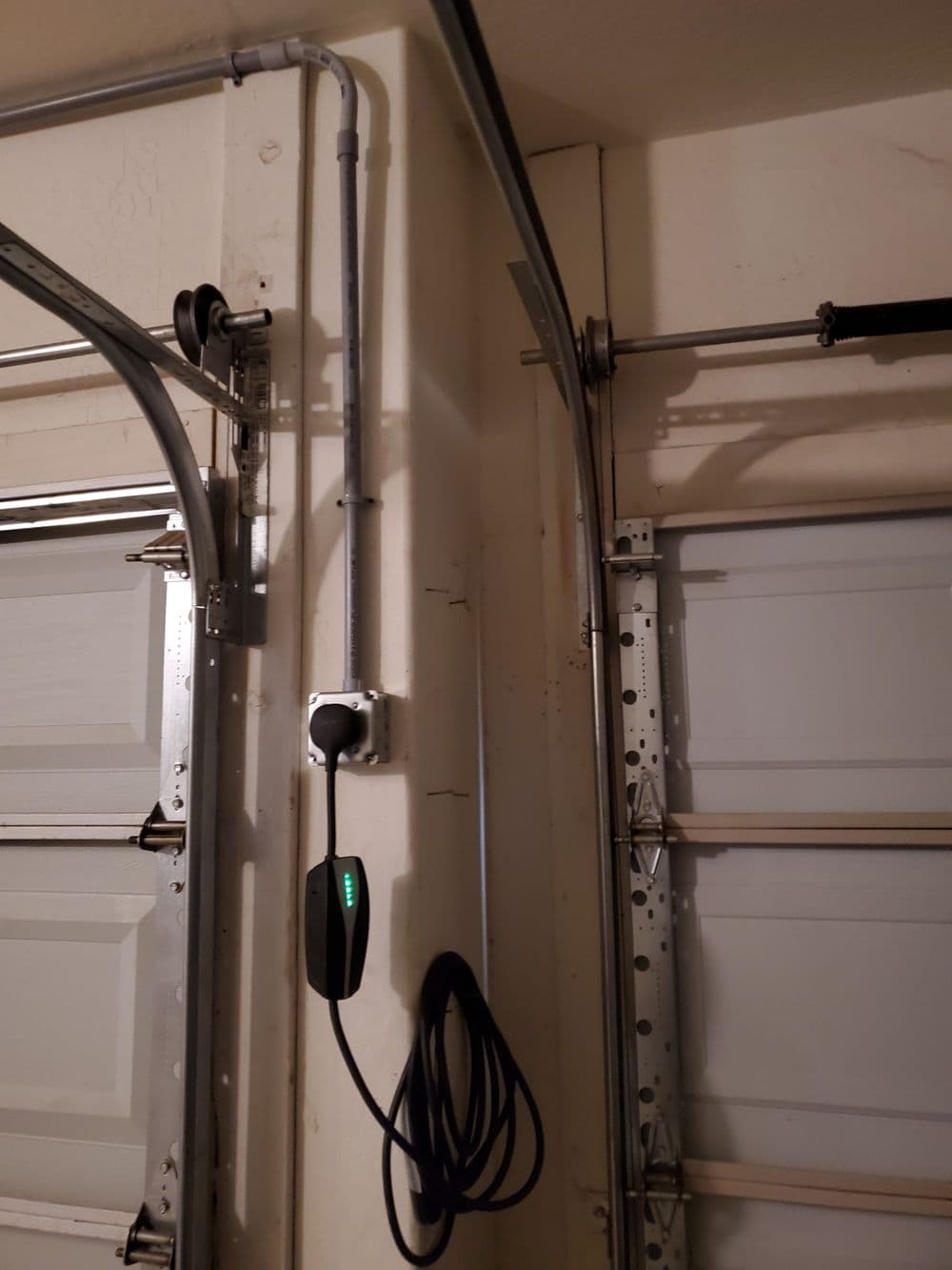 Electric car charger mounted on garage wall, with cables running along the ceiling.