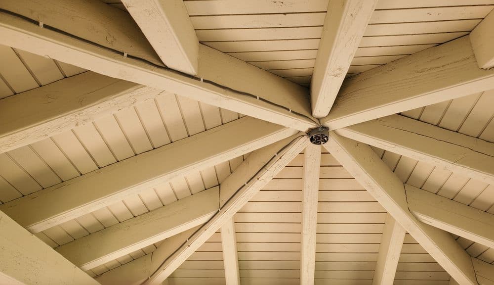 Interior view of a wooden gazebo ceiling showcasing intricate beam structure and warm colors.