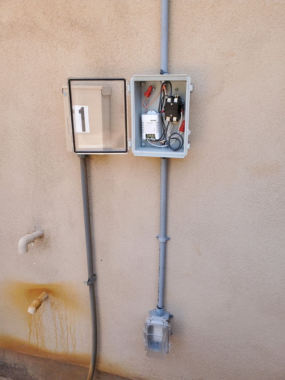 Electrical control box mounted on a wall with wiring and transparent cover.