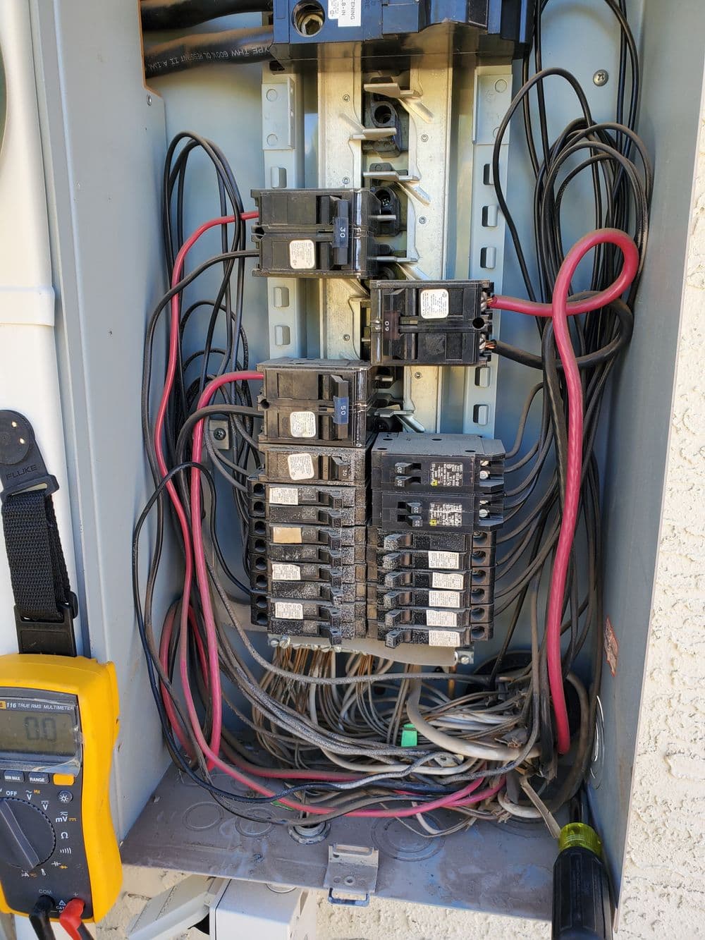 Electrical panel with circuit breakers, wires, and a multimeter for voltage testing.