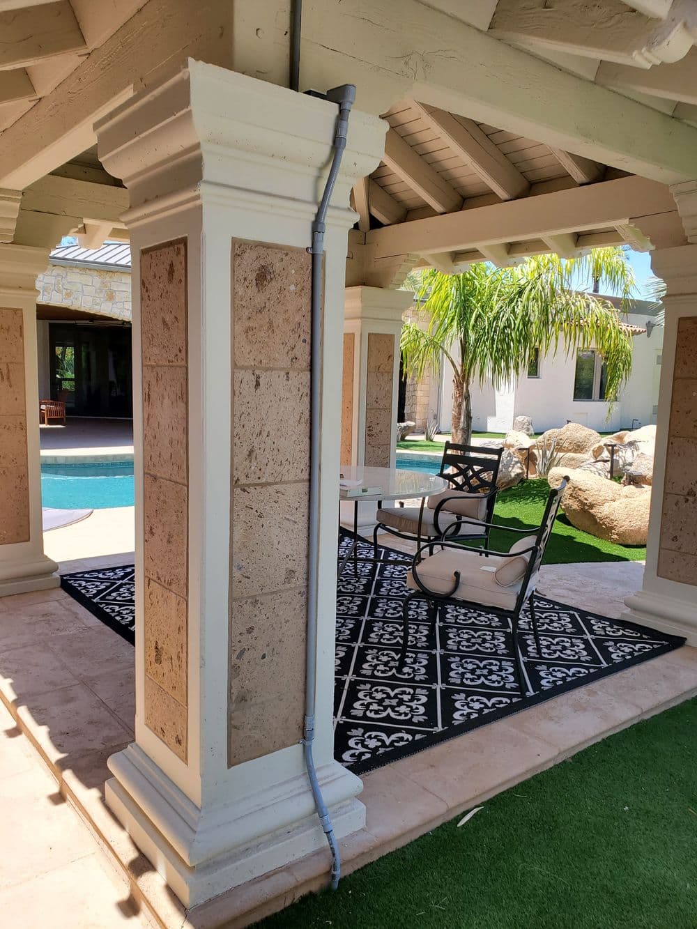 Luxe outdoor patio with columns, modern furniture, and a pool view in a sunny setting.