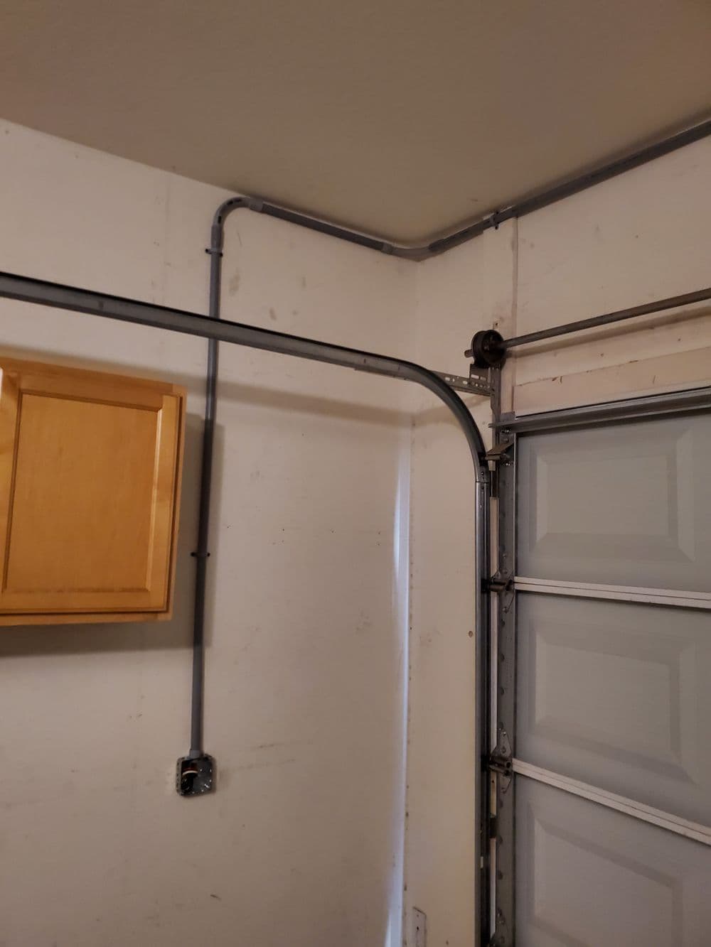 Garage interior showing wall-mounted pipe work and a wooden cabinet near the garage door.
