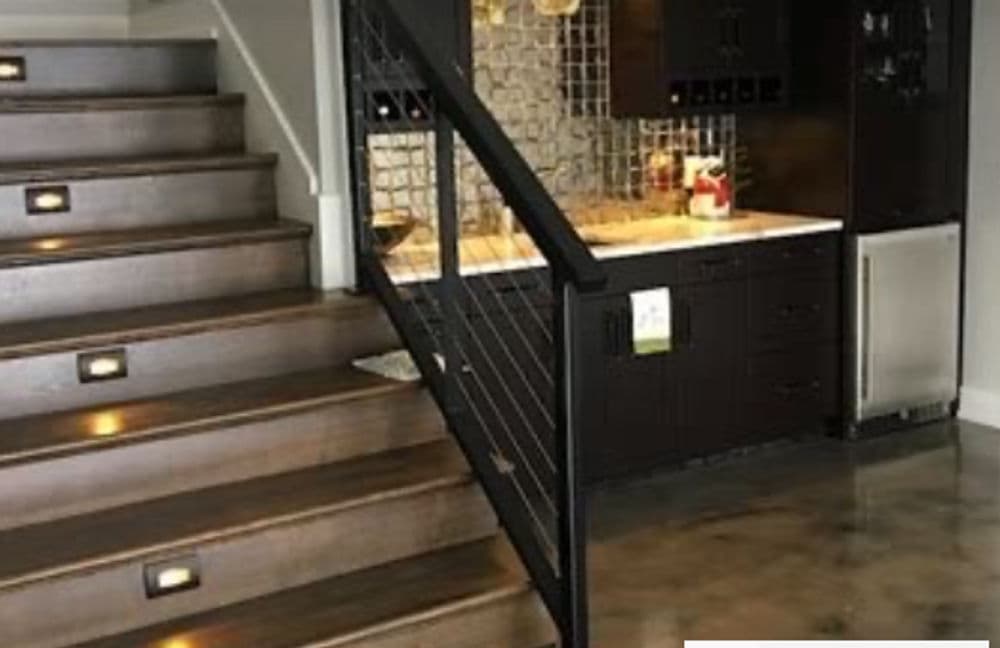 Modern staircase with led lighting leading to an open kitchen featuring dark cabinetry and tile backsplash.