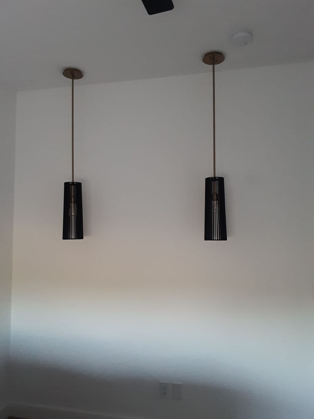 Two modern pendant lights with black shades hanging from the ceiling in a minimalist room.