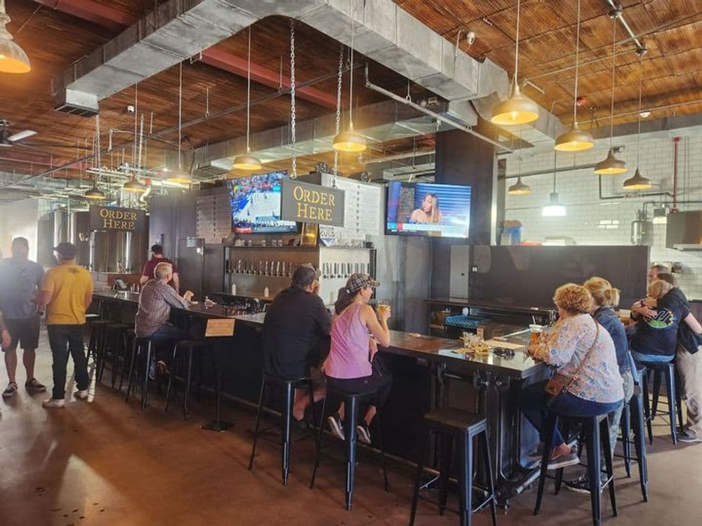 Modern bar interior with patrons seated, TVs showing sports and news, cozy ambiance.